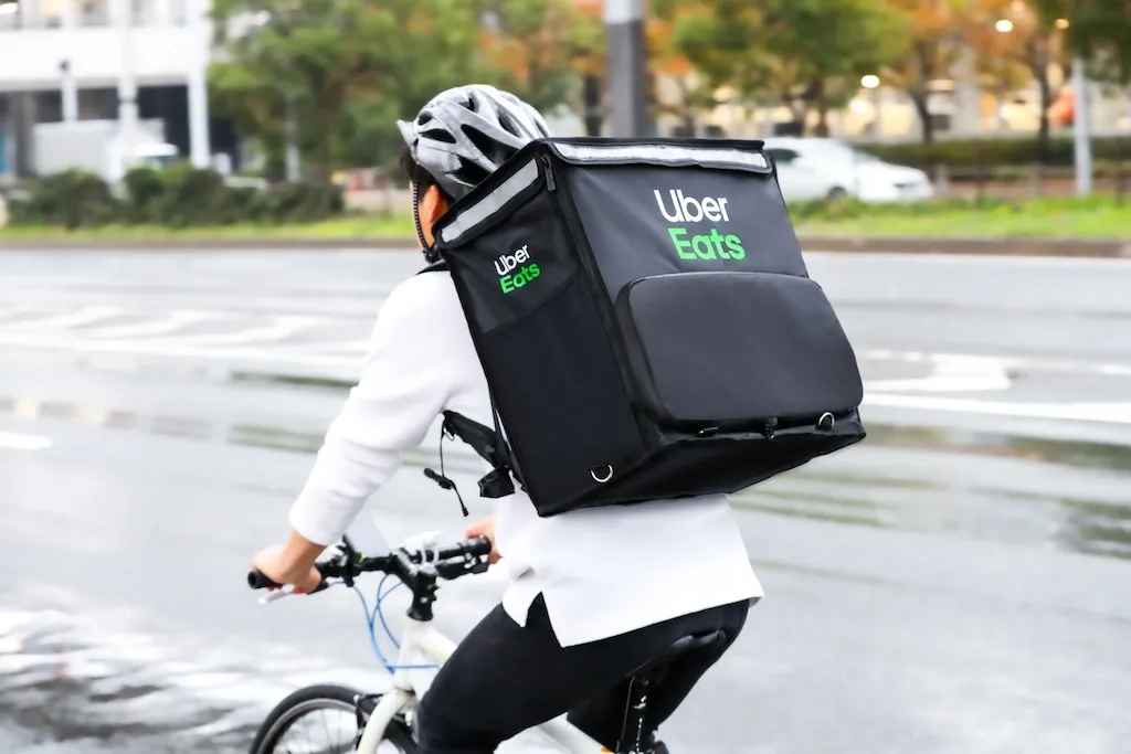 Uber Eats の配達バッグを背負って自転車で走る配達パートナー